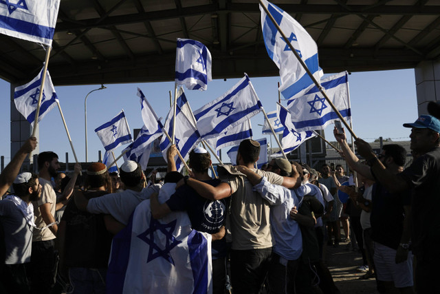 Para pengunjuk rasa melambaikan bendera nasional Israel untuk mendukung tentara yang diinterogasi atas pelecehan tahanan, di luar pangkalan militer Sde Teiman, Senin (29/7/2024). Foto: Tsafrir Abayov/AP Photo