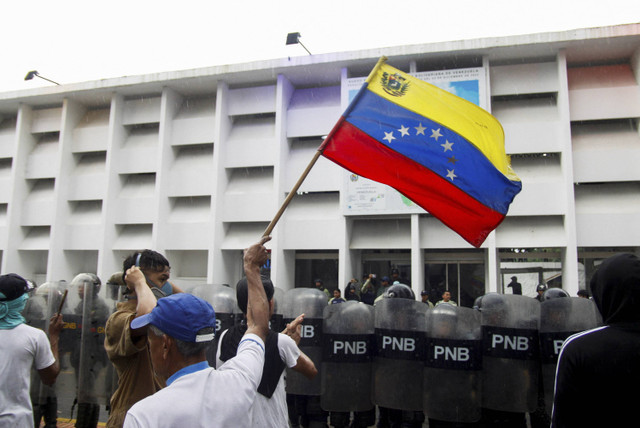 Seorang demonstran melambaikan bendera Venezuela di samping pasukan keamanan selama protes hasil pemilu setelah Presiden Venezuela Nicolas Maduro dan saingannya dari oposisi Edmundo Gonzalez mengklaim kemenangan di Venezuela, Minggu (29/7/2024). Foto: Samir Aponte/REUTERS