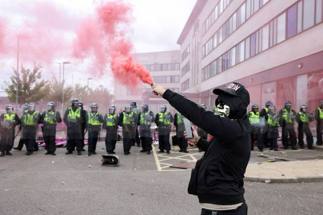 Seorang pengunjuk rasa menyalakan asap ketika petugas polisi berdiri di luar sebuah hotel, di Rotherham, Inggris, Minggu (4/8/2024). Foto: Hollie Adams/REUTERS