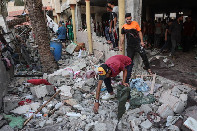 Orang-orang memilah-milah reruntuhan di dalam sekolah yang digunakan sebagai tempat penampungan sementara bagi para pengungsi Palestina setelah serangan Israel di Kota Gaza,  Sabtu (10/8/2024). Foto: Omar AL-QATTAA / AFP