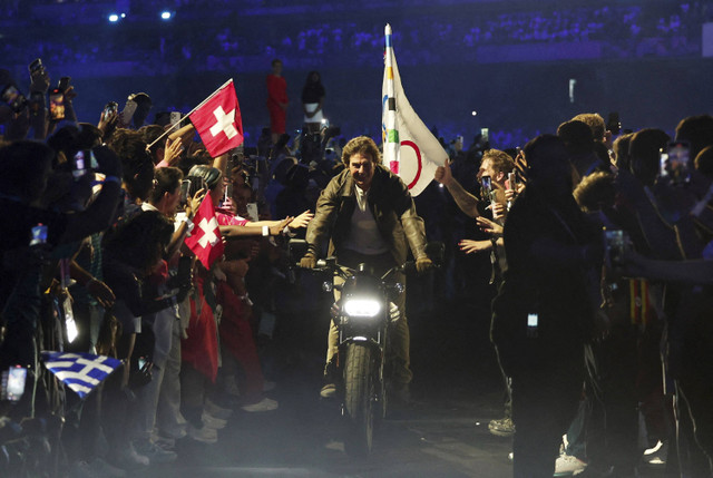 Aktor Tom Cruise mengendarai sepeda motor dengan bendera Olimpiade saat upacara penutupan Olimpiade Paris 2024 di Stade de France, Saint-Denis, Prancis, Minggu (11/8/2024). Foto: Gonzalo Fuentes/REUTERS 