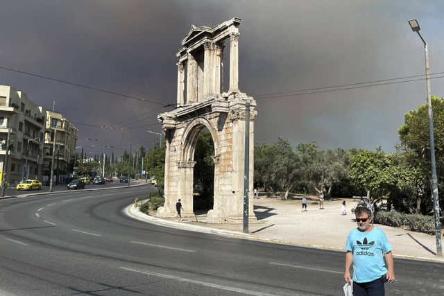 SAsap dari kebakaran hutan terlihat di atas Hadrian's Arch di pusat kota Athena, Minggu (11/8/2024). Foto: Derek Gatopoulos/AP Photo