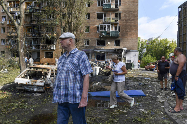 Orang-orang berjalan di dekat gedung apartemen yang rusak setelah ditembaki oleh pihak Ukraina, di Kursk, Rusia, Minggu (11/8/2024). Foto: AP Photo