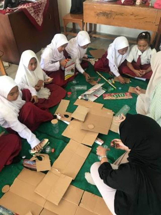 mahasiswa membantu memotong kardus dan botol bekas.