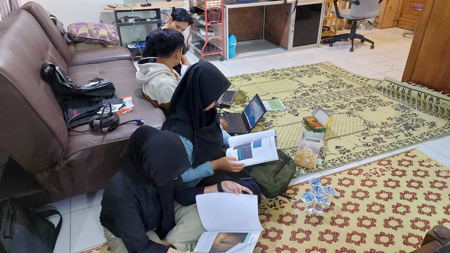 Anggota Karang Taruna berkumpul di rumah seorang warga Desa Mlopoharjo, dengan fokus pada booklet pembuatan web sederhana yang baru saja mereka terima.