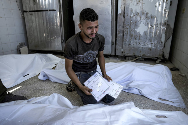 Seorang pria Palestina berduka atas anak kembarnya yang tewas dalam pemboman Israel di Jalur Gaza, sambil memegang akta kelahiran mereka, di kamar mayat rumah sakit di Deir al-Balah, Selasa, 13 Agustus 2024. Foto: AP Foto/Abdel Kareem Hana