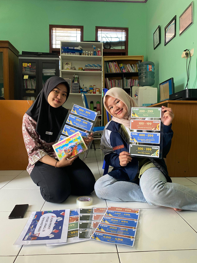 Mahasiswa TIM KKN II Universitas Diponegoro menyerahkan sekaligus menempelkan label klasifikasi pada staff Perpustakaan Taman Cerdas, Kel. Joglo sebagai program kerja monodisiplin Program Studi S1 Ilmu Perpustakaan, Surakarta, Rabu (31/07/2024)