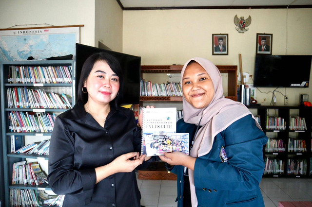 Berliana Rahmadhani (kanan) menyerahkan modul tentang perawatan bahan pustaka kepada Ibu Rinki, pustakawan Perpustakaan Kampung Mojosongo II, sebagai panduan praktis dalam menjaga koleksi perpustakaan.