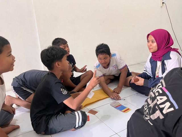 Fatma, mahasiswa Sastra Inggris KKN Undip mendampingi permainan kartu teka-teki bersama anak-anak RW 01 Kelurahan Sumber, Surakarta.