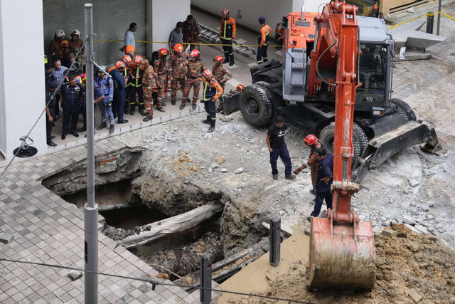 Petugas Pemadam Kebakaran dan Penyelamatan menggunakan derek untuk menggali setelah menerima laporan bahwa seorang wanita terjatuh ke dalam lubang runtuhan setelah bagian trotoar amblas di Kuala Lumpur, Jumat (23/8/2024). Foto: Vincent Thian/AP PHOTO