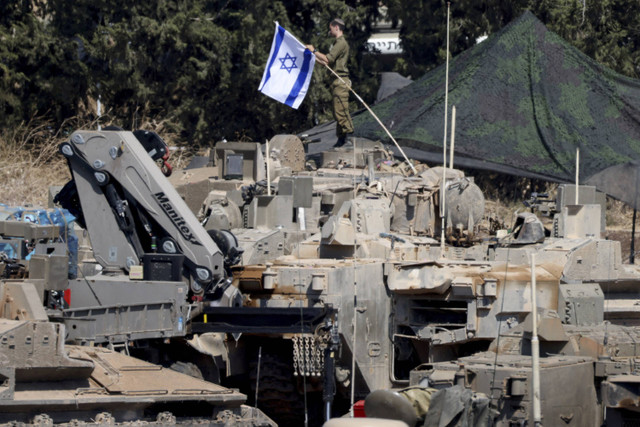 Seorang anggota militer Israel mengatur bendera Israel saat kendaraan lapis baja diatur dalam formasi, di tengah permusuhan lintas batas antara Hizbullah dan Israel, di Israel utara, Senin (30/9/2024). Foto: Gil Eliyahu/REUTERS