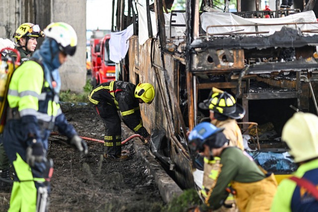 Petugas pemadam kebakaran dan petugas penyelamat berdiri di samping bus yang terbakar yang membawa para siswa dan guru di pinggiran Bangkok, pada 1 Oktober 2024. Foto: Manan Vatsanyaya/AFP