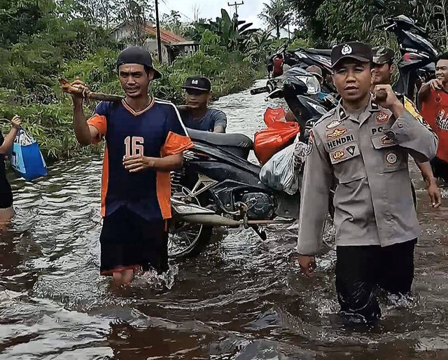 - Bhabinkamtibmas Polsek Dedai Aipda Hendri memikul kendaraan warga melewati banjir di Desa Lundang Baru. Foto: Dok. Polres Sintang