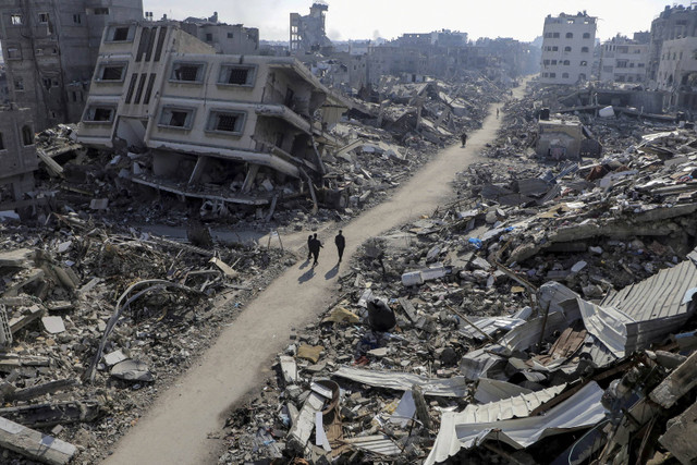 Warga Palestina berjalan melewati rumah-rumah yang hancur, di tengah konflik yang sedang berlangsung antara Israel dan Hamas, di kamp pengungsi Jabalia, di Jalur Gaza utara (22/2/2024). Foto: Mahmoud Issa/REUTERS