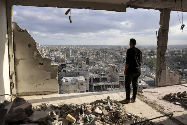 Seorang pria berdiri di atas sebuah bangunan yang rusak parah dan melihat bangunan lain yang hancur di Khan Yunis, Jalur Gaza selatan, Senin (7/10/2024). Foto: Bashar Taleb/AFP