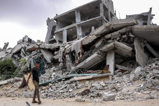 Seorang pemuda berjalan melewati sebuah bangunan yang hancur di Khan Yunis di Jalur Gaza selatan, Senin (7/10/2024). Foto: Bashar Taleb/AFP