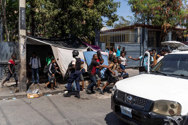 Orang-orang berjalan melewati Polisi Nasional Haiti ketika mereka berusaha mengusir geng di sebuah lingkungan dekat Istana Kepresidenan di pusat Port-au-Prince, Haiti pada tanggal 3 Maret 2023. Foto: Richard Pierrin / AFP