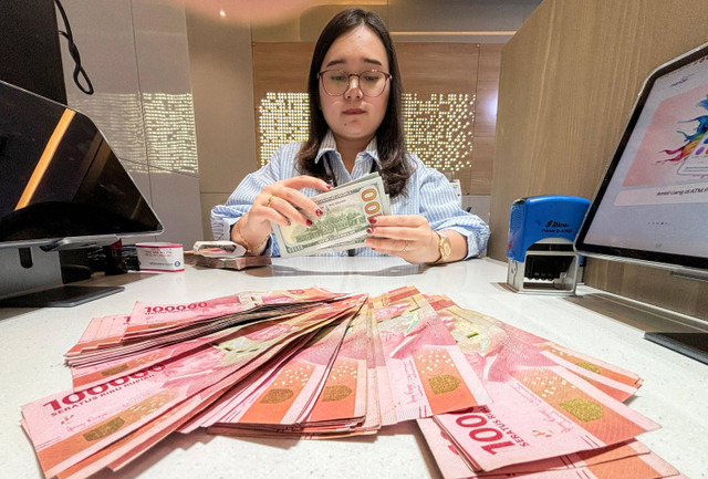 Petugas menunjukkan uang pecahan dolar AS dan rupiah di Bank Mandiri, Jakarta, Jumat (11/10/2024).  Foto: ANTARA FOTO/Rivan Awal Lingga