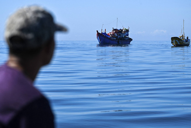 Seorang pria di atas kapal melihat para pengungsi Rohingya di atas kapal yang berlabuh di lepas pantai Labuhan Haji, Provinsi Aceh Selatan, Selasa (22/10/2024). Foto: Chaideer Mahyuddin/AFP