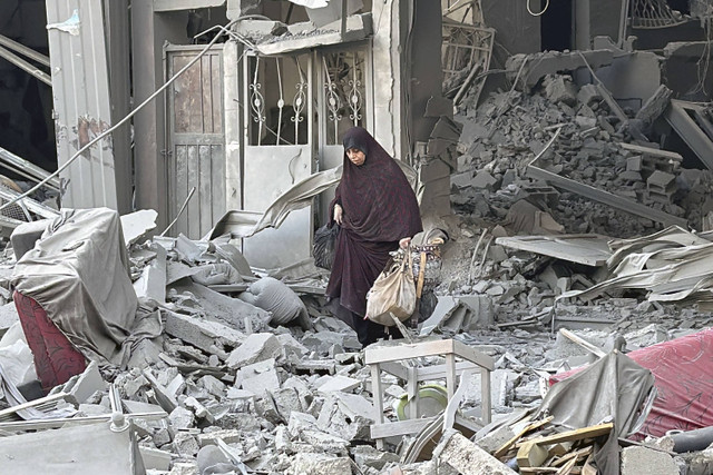 Seorang wanita berjalan di atas reruntuhan bangunan setelah serangan Israel di Beit Lahia di Jalur Gaza utara, Senin (28/10/2024). Foto: AFP