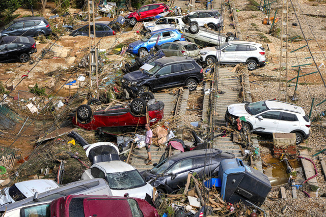 Seorang pria berdiri di antara tumpukan mobil yang terendam banjir di Valencia, Spanyol, Kamis, 31 Oktober 2024. Foto: AP Photo/Manu Fernandez