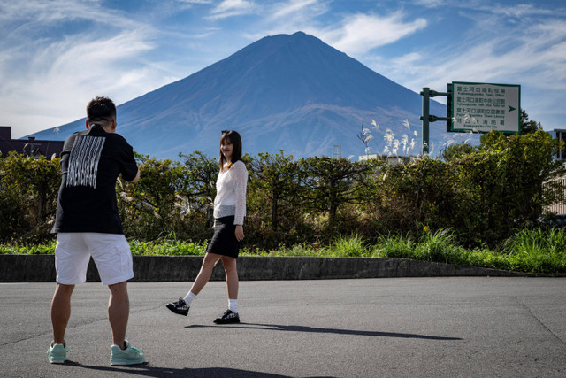 Warga mengambil foto dengan latar belakang Gunung Fuji yang tidak tertutupi salju di Fujikawaguchiko, prefektur Yamanashi, Jepang, Kamis (31/10/2024). Foto: Yuichi YAMAZAKI / AFP