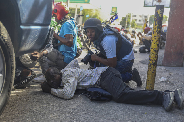 Jurnalis berlindung dari baku tembak antara geng dan polisi di Port-au-Prince, Haiti, Senin, 11 November 2024. Foto: AP Photo/Odelyn Joseph