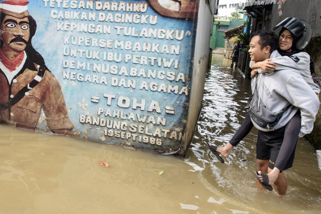 Warga menggendong pasangannya berjalan melintasi banjir di Dayeuhkolot, Kabupaten Bandung, Jawa Barat, Jumat (22/11/2024). Foto: ANTARA FOTO/Novrian Arbi