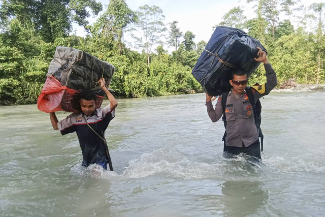 Petugas melewati sungai dan lembah saat mengawal dan mengamankan distribusi logistik Pilkada di sejumlah wilayah di Provinsi Maluku, Senin (26/11/2024). Foto: Dok. Polda Maluku