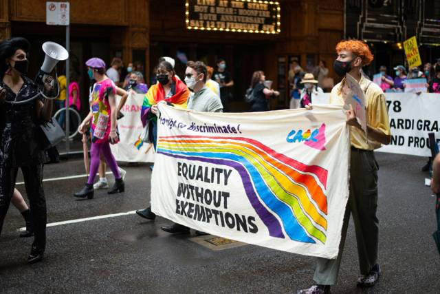 Image Sumber : https://unsplash.com/photos/a-group-of-people-walking-down-a-street-holding-a-banner-43b5JNIKsDk