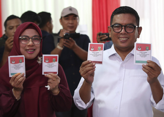 Calon Gubernur Banten Andra Soni (kanan) didampingi istri Tinawati (kiri) menunjukan surat suara sebelum melakukan pencoblosan di TPS 29 Peninggilan, Ciledug, Kota Tangerang, Banten, Rabu (27/11/2024). Foto: Muhammad Iqbal/ANTARA FOTO