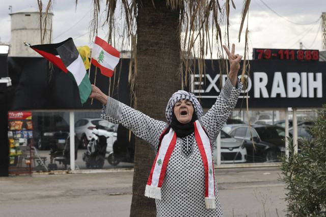 Seorang wanita melambaikan bendera Lebanon dan Palestina saat ia menyapa orang-orang di kota Sidon, Lebanon selatan, pada 27 November 2024. Foto: AFP