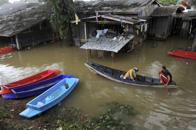 Pada tanggal 29 Desember 2014, seorang penduduk desa di Thailand mendayung perahu di tengah banjir di dekat perbatasan Thailand-Malaysia di Narathiwat. Foto: MADAREE TOHLALA/AFP