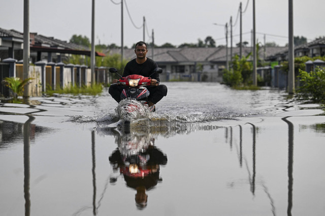 Seorang pria mengendarai sepeda motor di tengah banjir setelah hujan deras di Pasir Mas, negara bagian Kelantan, Malaysia, Selasa (3/12/2024). Foto: Hasnoor Hussain/REUTERS