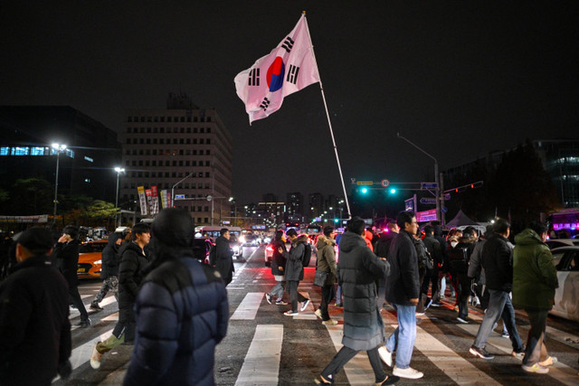 Warga berkumpul setelah Presiden Korea Selatan Yoon Suk Yeol mengumumkan darurat militer di depan gerbang utama Majelis Nasional di Seoul, Korea Selatan, Selasa (3/12/2024). Foto: Anthony Wallace/AFP