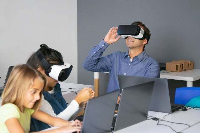 sumber: https://www.freepik.com/free-photo/middle-aged-teacher-testing-vr-headset-smiling_11072746.htm#fromView=search&page=1&position=48&uuid=6ac3f434-7f0c-4f9f-8cee-d94e12e5c863, ilustrasi pengguna teknologi dibidang pendidikan.