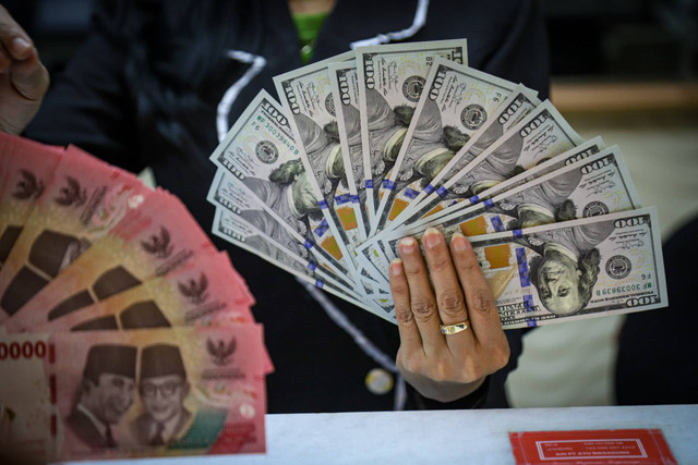 Seorang petugas menunjukan pecahan Dolar AS dan Rupiah di salah satu tempat penukaran mata uang asing di Kwitang, Jakarta, Senin (9/12/2024). Foto: Iqbal Firdaus/kumparan