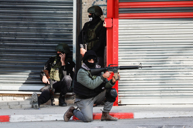 Seorang anggota pasukan keamanan Palestina mengarahkan senjata saat bentrokan dengan militan di kamp Jenin di Tepi Barat yang diduduki Israel, 14 Desember 2024. Foto: Reuters/Raneen Sawafta