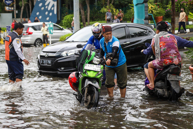 Pengendara mendorong motornya saat melintasi banjir rob yang melanda kawasan Pluit, Penjaringan, Jakarta Utara, Senin (16/12/2024). Foto: Iqbal Firdaus/kumparan