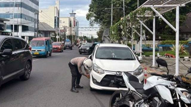 Polisi melakukan penggembosan ban kendaraan yang parkir sembarangan di area jalan utama di Kota Manado, Sulawesi Utara. (foto: istimewa)