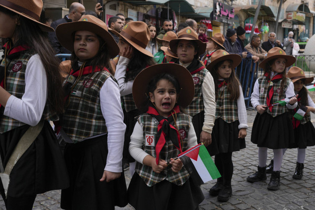 Seorang pramuka menangis sambil memegang bendera Palestina selama prosesi tradisional Kristen menuju Gereja Kelahiran yang secara tradisional diyakini sebagai tempat kelahiran Yesus, pada Malam Natal di Bethlehem, Selasa (24/12/2024). Foto: Matias Delacroix/AP Photo