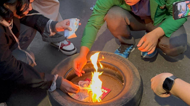 Massa Aksi tolak PPN 12% melemparkan uang mainan dan bakar ban menggunakan uang mainan tersebut di Patung Kuda, Jakarta pada Jumat (27/12). Foto: Abid Raihan/kumparan