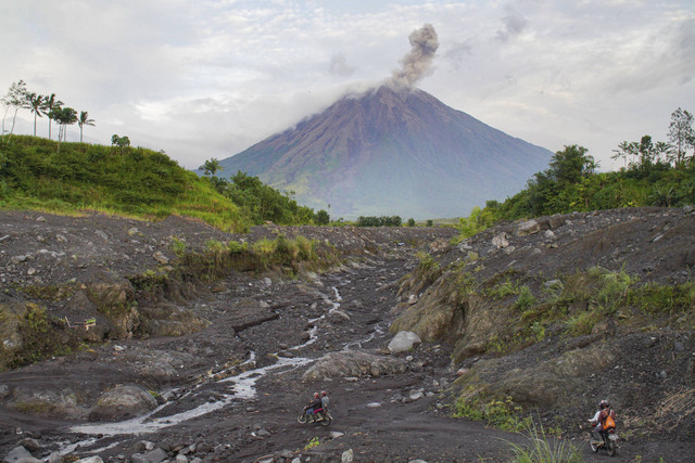 Warga melintasi jalur Curah Kobokan saat asap vulkanis keluar dari kawah Gunung Semeru terlihat dari Desa Supiturang, Lumajang, Jawa Timur, Sabtu (28/12/2024).  Foto: Irfan Sumanjaya/ANTARA FOTO