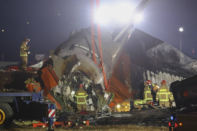 Petugas pemadam kebakaran dan petugas penyelamat bekerja di dekat lokasi kecelakaan pesawat Jeju Air Boeing 737-800 di Bandara Internasional Muan di Provinsi Jeolla Selatan, Korea Selatan, Minggu (29/12/2024). Foto: Yonhap via AFP