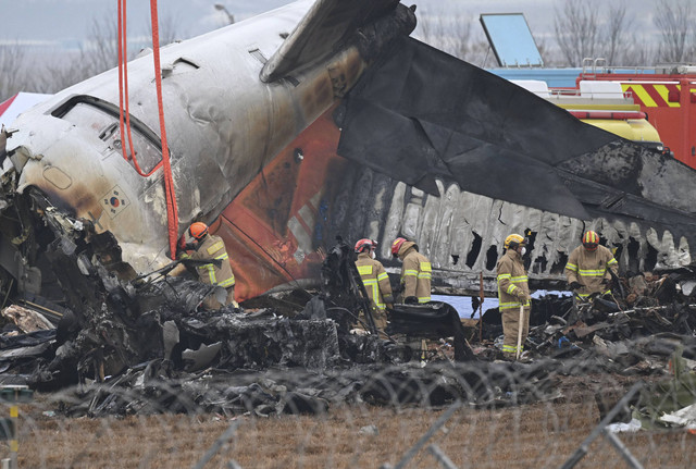 Petugas pemadam kebakaran dan petugas penyelamat bekerja di dekat lokasi kecelakaan pesawat Jeju Air Boeing 737-800 di Bandara Internasional Muan di Provinsi Jeolla Selatan, Korea Selatan, Minggu (29/12/2024). Foto: Jung Yeon-je/AFP