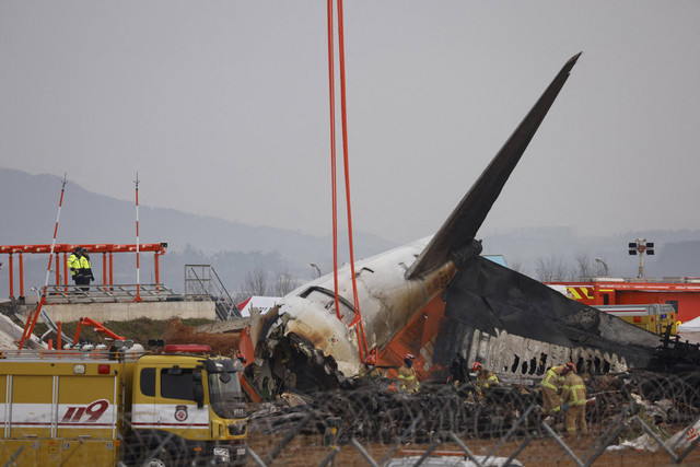 Petugas pemadam kebakaran dan petugas penyelamat bekerja di dekat lokasi kecelakaan pesawat Jeju Air Boeing 737-800 di Bandara Internasional Muan di Provinsi Jeolla Selatan, Korea Selatan, Minggu (29/12/2024). Foto: Kim Soo-Hyeon/REUTERS