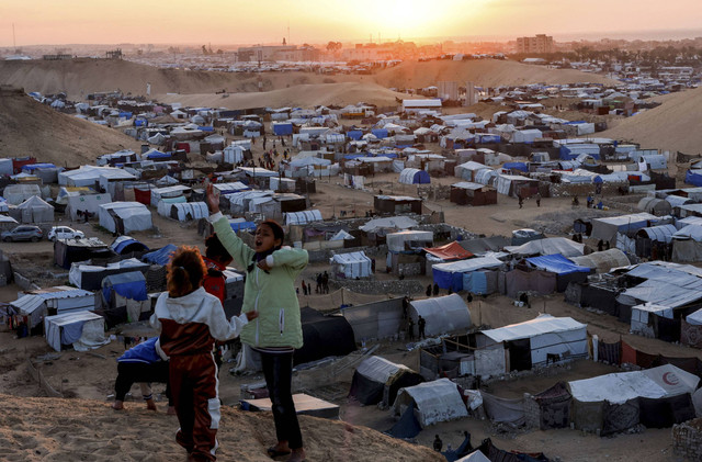 Anak-anak Palestina yang mengungsi berbicara satu sama lain saat mereka berlindung di sebuah kamp tenda, di tengah konflik yang sedang berlangsung antara Israel dan Hamas, di Khan Younis, Jalur Gaza selatan, Minggu (29/12/2024). Foto: Mohammed Salem/REUTERS