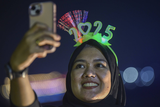 Warga mengenakan bando bertuliskan "2025" saat malam perayaan tahun baru 2025 di tepian Sungai Mahakam, Samarinda, Kalimantan Timur, Rabu (1/1/2025). Foto: M Risyal Hidayat/ANTARA FOTO