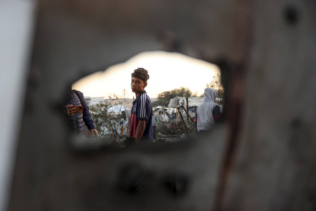 Seorang anak laki-laki Palestina yang mengungsi berdiri di antara tenda-tenda yang rusak usai serangan Israel terhadap kamp pengungsian sementara di Mawasi Khan Yunis di Jalur Gaza selatan, Kamis (2/1/2025). Foto: Bashar Taleb/AFP