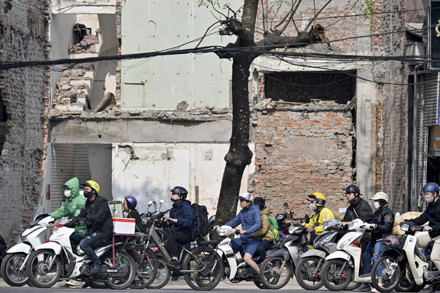 Orang-orang mengendarai sepeda motor di depan rumah-rumah tua yang sedang dihancurkan di Hanoi (6/1/2025). Foto: Nhac NGUYEN/AFP